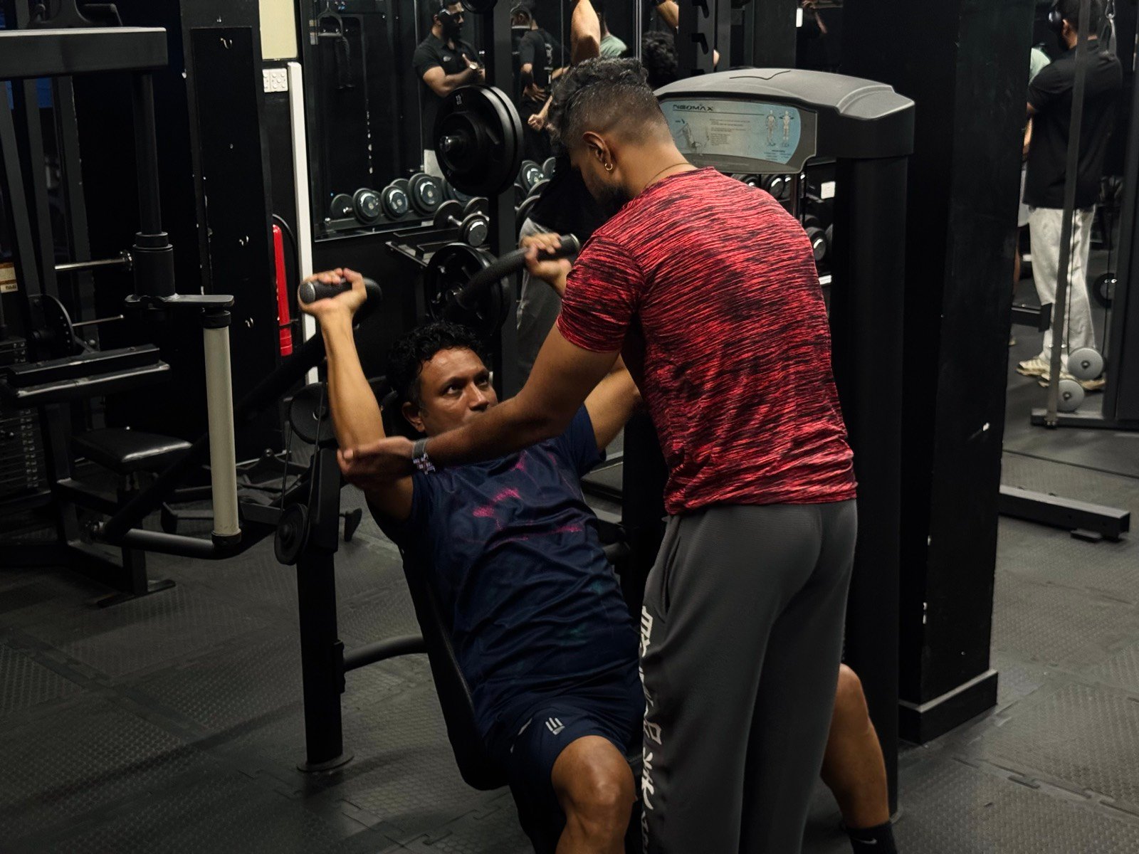 A trainer counting reps beside a seated press machine